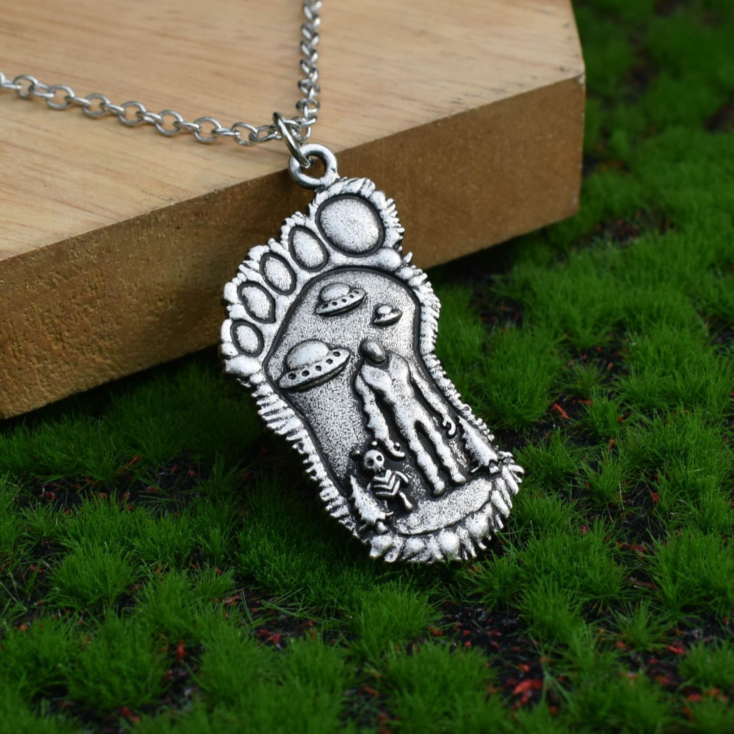 Silver Bigfoot Necklace with Alien Buddy Pendant on a table