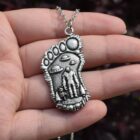Silver Bigfoot Necklace with Alien Buddy Pendant in a hand