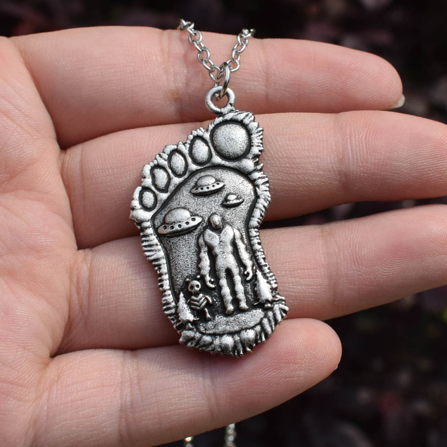 69b85261-1c1d-4df2-ad66-45f4b3194ef5.jpg Silver Bigfoot Necklace with Alien Buddy Pendant in a hand